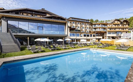 Hotel mit Pool und Liegewiese vor bewaldeter Bergkulisse