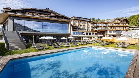 Hotel mit Pool und Liegewiese vor bewaldeter Bergkulisse