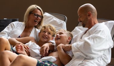 Family in bathrobes laughing and relaxing on lounge chairs