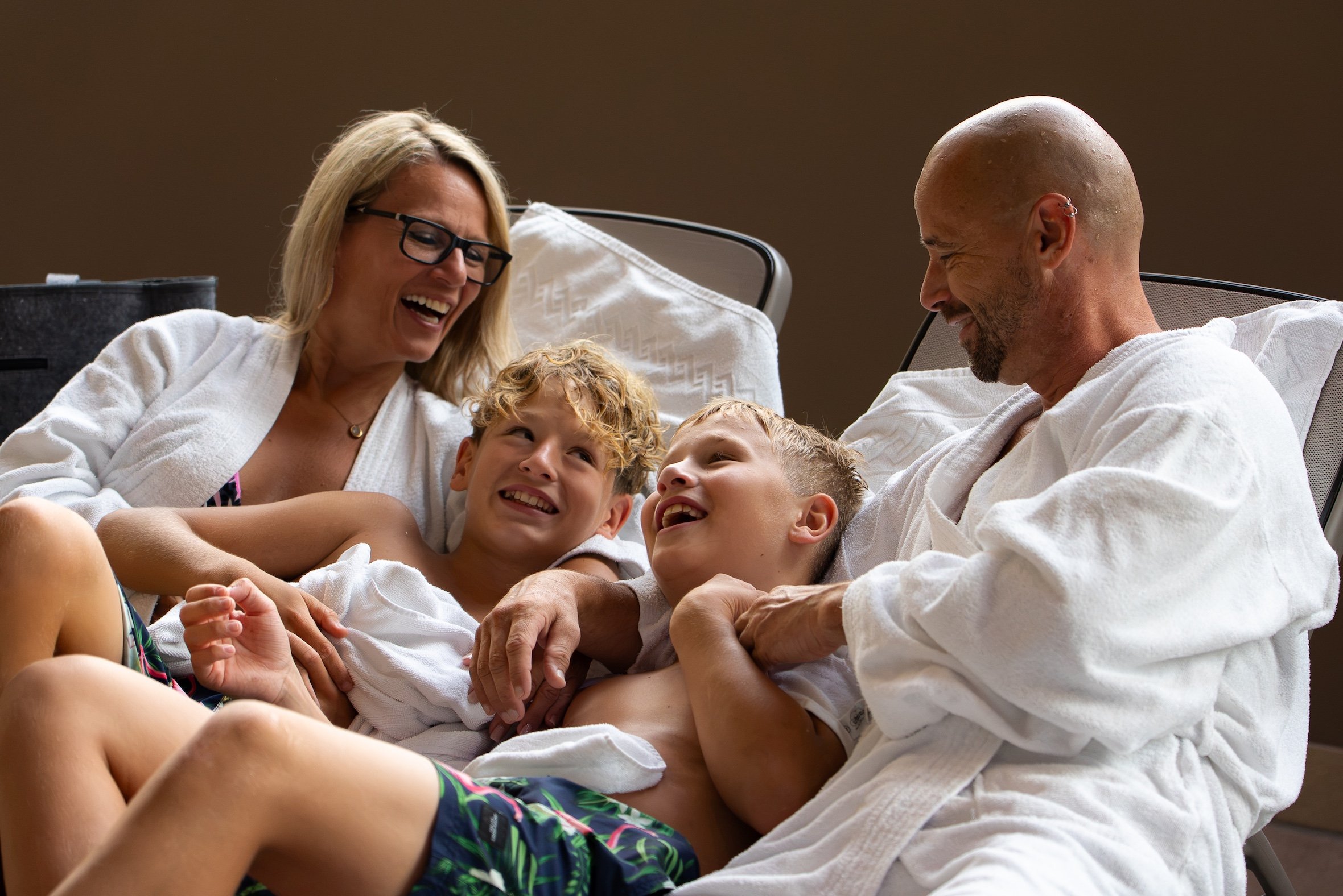 Family in bathrobes relaxing and laughing together on lounge chairs