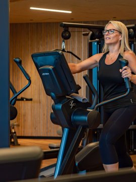 Frau trainiert auf einem Crosstrainer in einem Fitnessstudio mit Holzvertäfelung