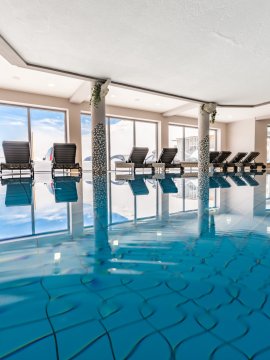 Indoorpool mit Liegen und Panoramafenstern bei Tageslicht