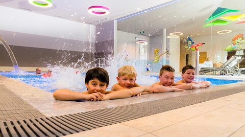 Vier Jungs planschen am Beckenrand vom Familien-Spaßbad