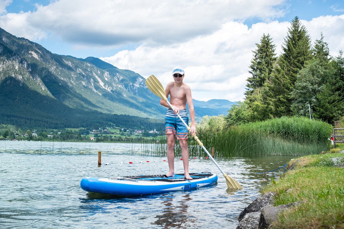 Stand-up paddler near shore with mountain view and reeds