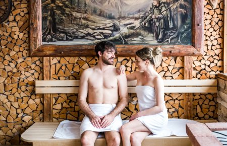 Paar sitzt entspannt in Sauna mit Wandbild und Holzscheitdekor