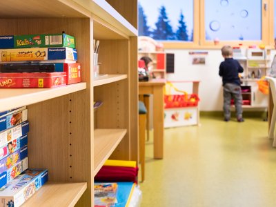 Regal mit Brettspielen in Spielraum mit Kindern am Fenster