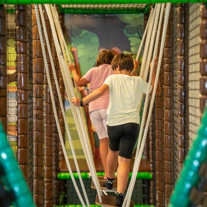 Zwei Kinder balancieren im Indoor-Spielplatz auf schwingender Seilbrücke