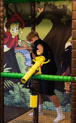 Junge spielt mit gelbem Ballwerfer vor bunter Wand mit Comicfiguren im Spielbereich