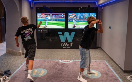 Two boys play an interactive baseball video game in front of two screens in a room.
