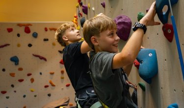Zwei Jungen klettern an einer bunten Kletterwand in einer Halle