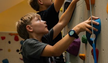 Zwei Jungen klettern an einer bunten Kletterwand in einer Halle nach oben