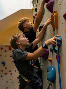 Two boys climbing up a colorful indoor climbing wall