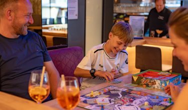 Junge und Erwachsene sitzen an einem Tisch und spielen ein Brettspiel in einer Bar oder einem Café.