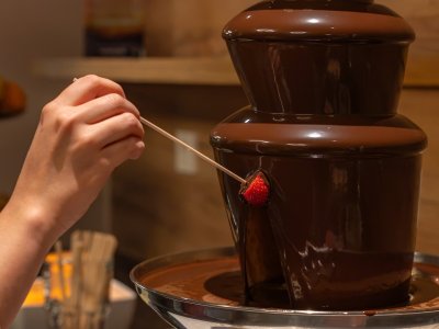 Hand dipping strawberry on skewer into chocolate fountain