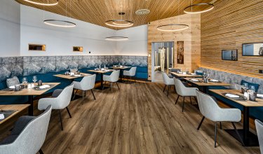Spacious restaurant with wooden ceiling, designer lights and mountain motif upholstery