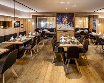 Holzvertäfeltes Restaurant mit Skisprungbild und liebevoll gedeckten Tischen
