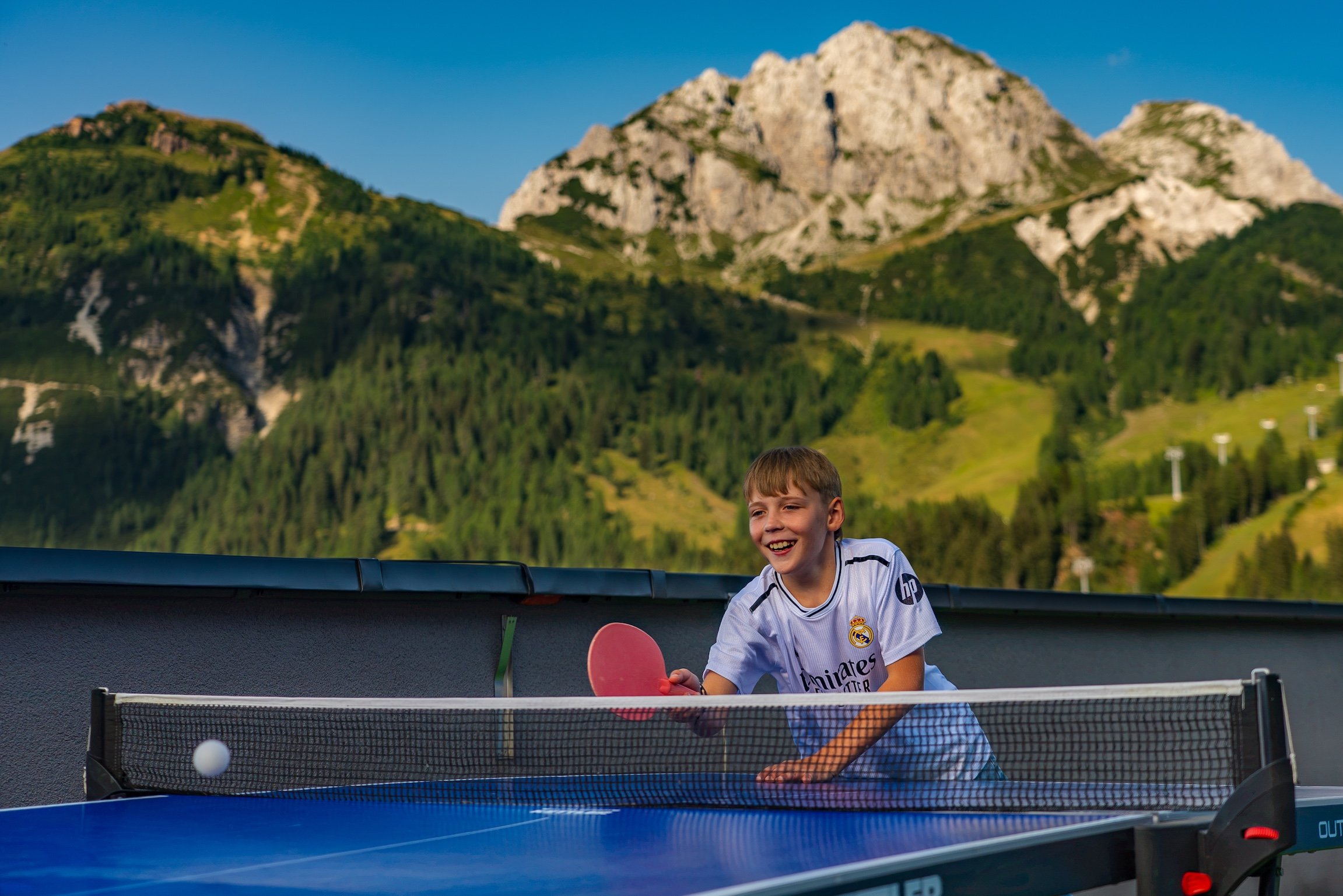 Boy playing table tennis outdoors with mountains in the background