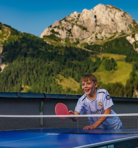 Boy playing table tennis outdoors with mountains in the background