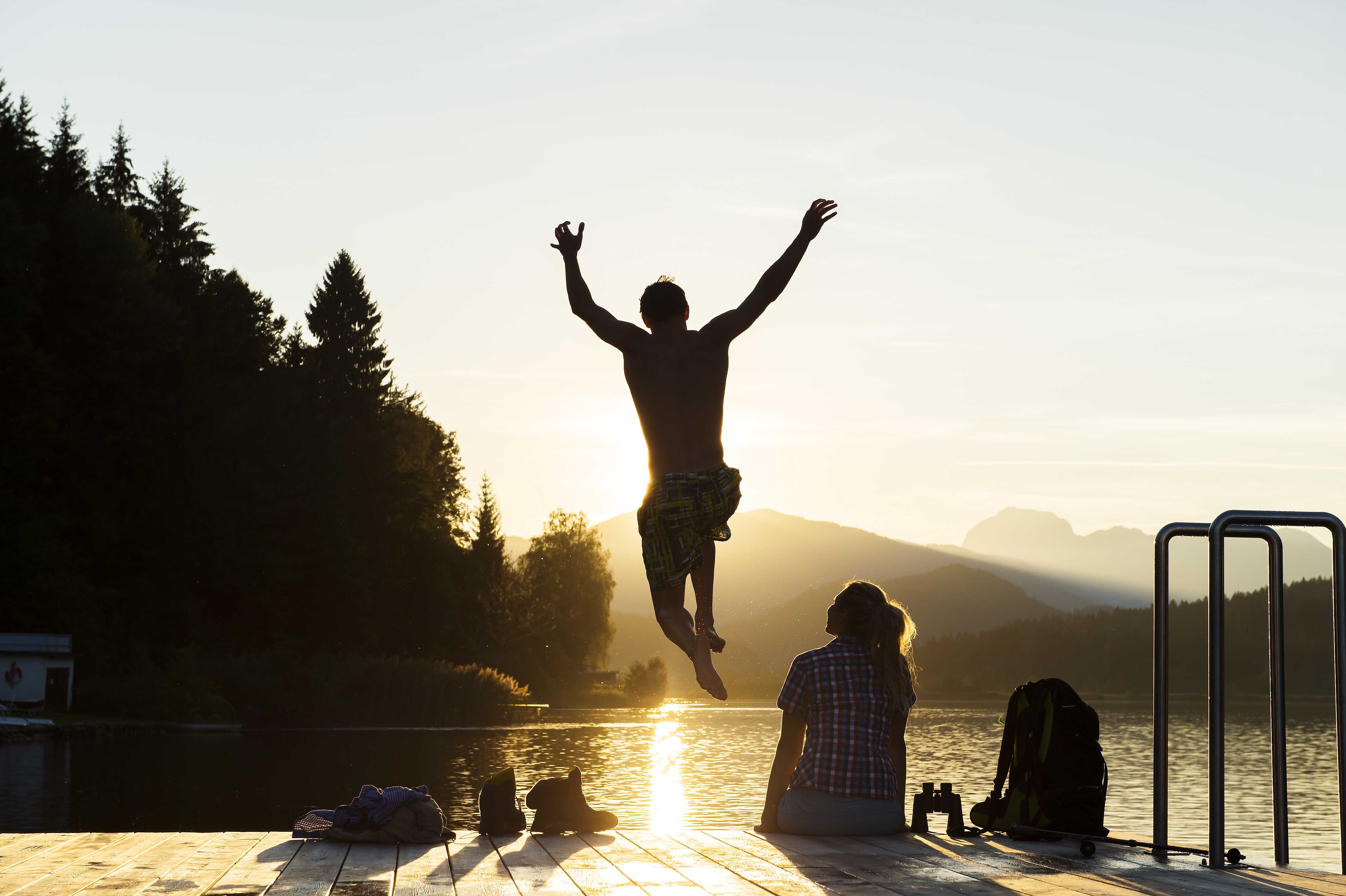 Sonnenuntergang am Steg, Person springt ins Wasser, Paar sitzt am Ufer