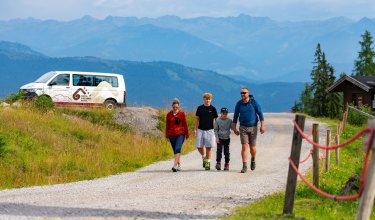 Family hiking on a mountain path with Hotel Gartner Kofel van and alpine mountains in the background
