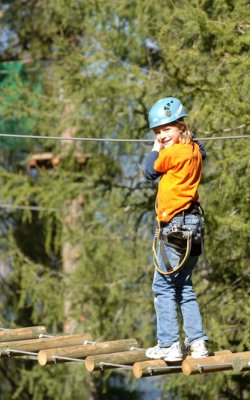 Kind mit Helm balanciert auf Hängebrücke im Hochseilgarten