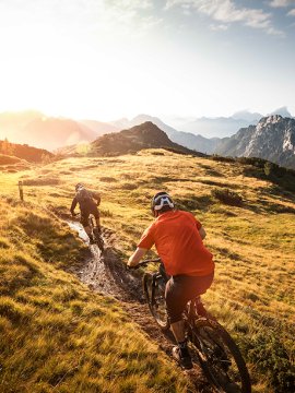 Zwei Mountainbiker fahren bei Sonnenuntergang auf einem Bergrücken
