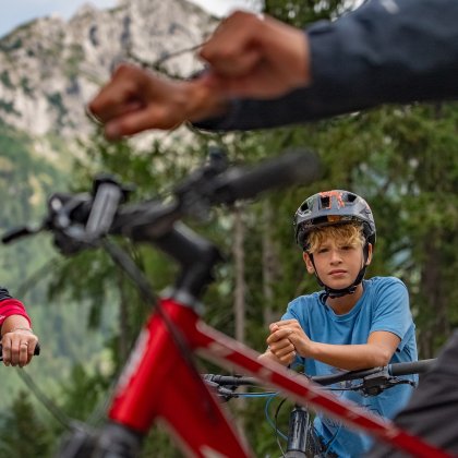 Junge mit Helm und blauem Shirt sitzt auf Fahrrad, im Vordergrund zwei Fäuste zum Abklatschen