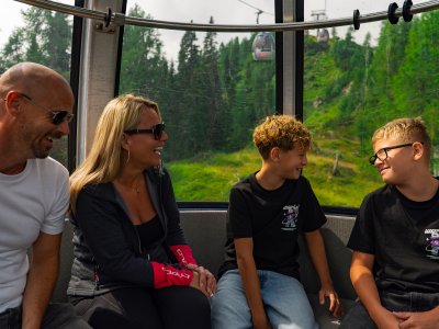 Four people sitting in a gondola, laughing and looking at each other, green mountains outside