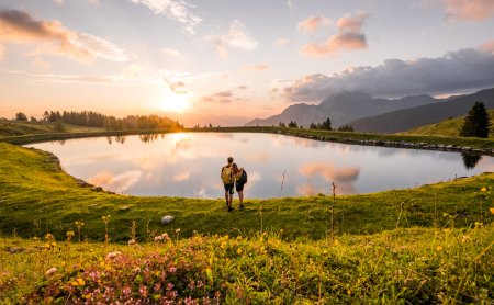 Wanderpaar am See bei Sonnenuntergang inmitten blühender Wiese