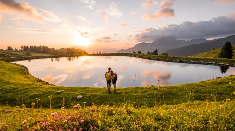 Wanderpaar am See bei Sonnenuntergang inmitten blühender Wiese
