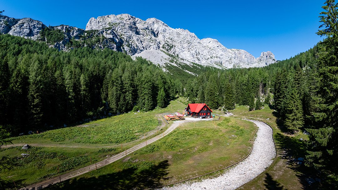 Red mountain hut in forest clearing with panoramic mountain backdrop