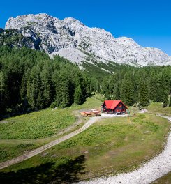 Rote Berghütte in Waldlichtung mit Gebirgspanorama im Hintergrund