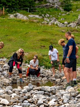 Gruppe von Menschen steht und hockt um einen kleinen Wasserpool in felsiger Wiese