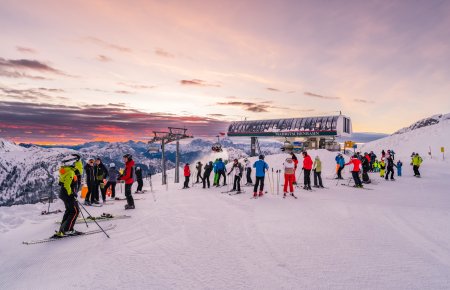 Skiers wait in line in front of the ski lift at sunrise.