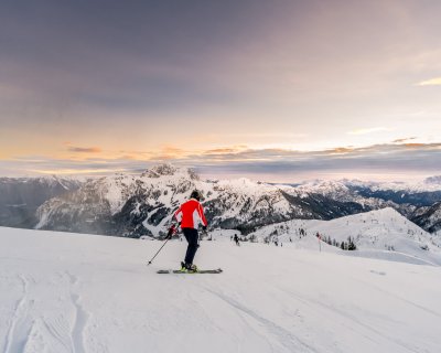 Skifahrer auf der Piste im Sonnenaufgang, Bergpanorama im Hintergrund.