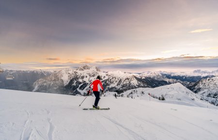 Skier on the slope at sunrise, mountain panorama in the background.