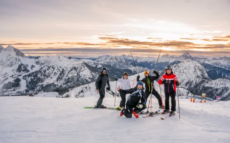 Five skiers posing together on the slope at sunrise, mountains in the background.