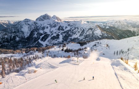 Drei Skifahrer fahren den Berg hinab, im Hintergrund ist das Bergpanorama zu sehen.