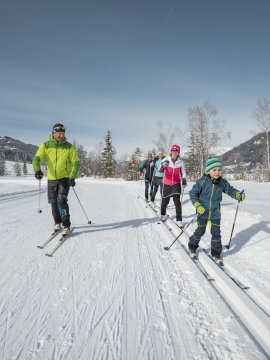 Familie beim Langlaufen auf einer verschneiten Strecke in den Alpen.
