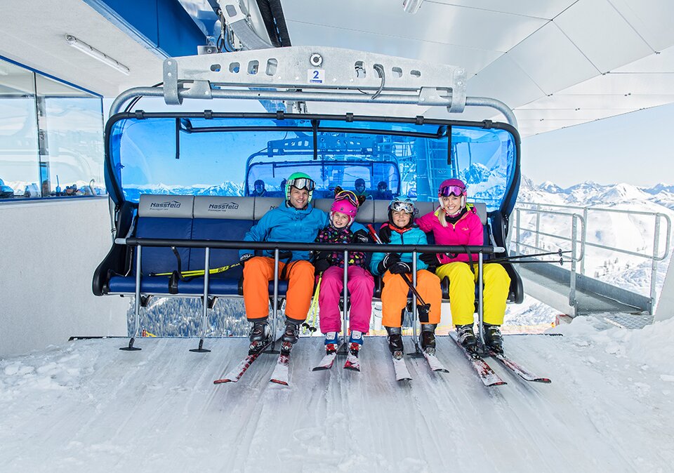 Familie in knallbunten Skianzügen kommt mit dem Sessellift an