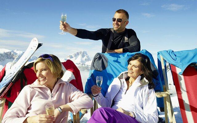 Skifahrer trinken Sekt auf Liegestühlen am Berg
