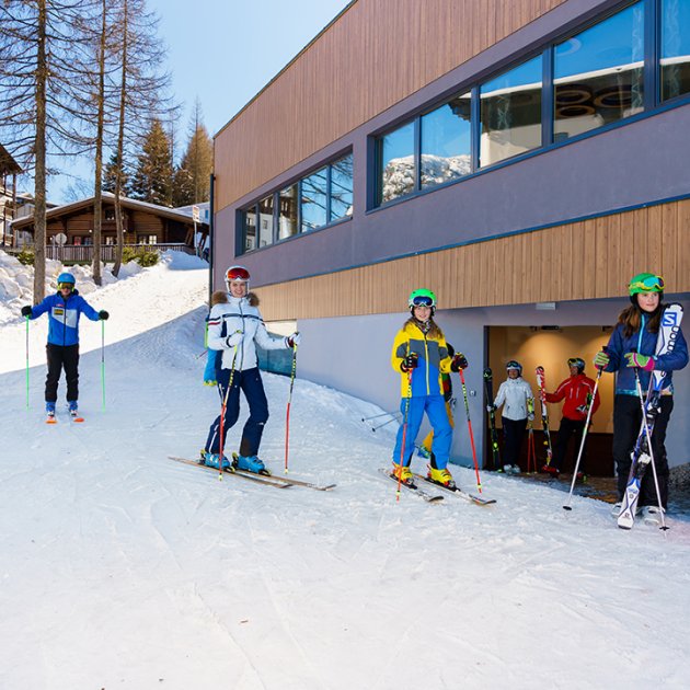 Skifahrer und Skifahrerinnen vor einem Gebäude am Hang.