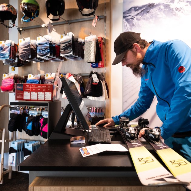 Verkäufer im Skishop arbeitet am Computer, Ski liegen auf dem Tisch.