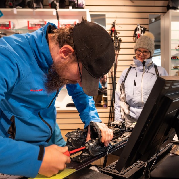 Der Verkäufer repariert Ski, während eine Kundin zuschaut.
