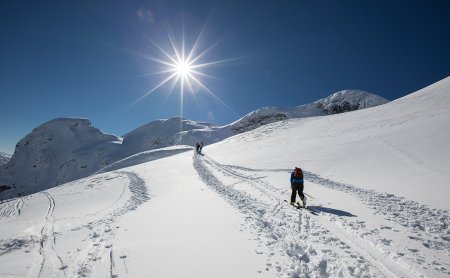 Zwei Personen gehen mit Tourenski durch den tiefen Schnee unter der Sonne.