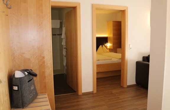 Blick auf zwei offene Türen in einem Flur, links Badezimmer, rechts Schlafzimmer mit Bett und Holzmöbeln