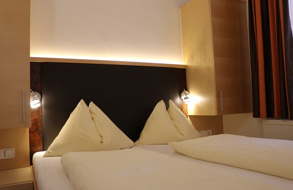 Doppelbett mit beigen Kissen und Decken, beleuchteter Kopfteil und Holzschränke an den Seiten