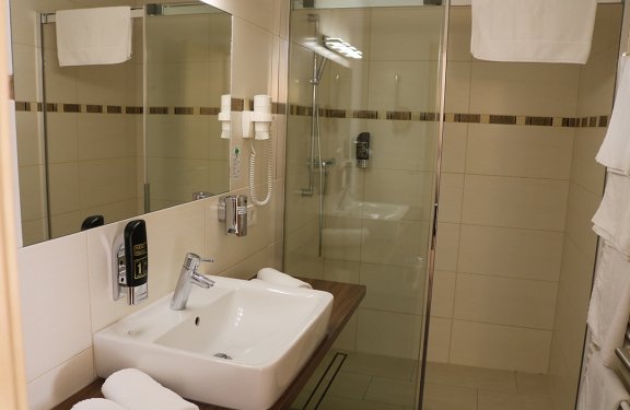 Moderner Badezimmerwaschbecken mit Spiegel, Handtüchern und Duschkabine mit Glaswand