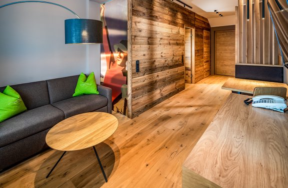 Moderner Raum mit grauem Sofa, grünem Kissen, Holzwand und Holzboden