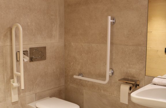 Barrierefreies Badezimmer mit Wandtoilette, Haltegriffen und Waschbecken mit Spiegel